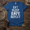 Eat Sleep Rope Repeat text design with a silhouette of a cowboy roping a calf, on a blue t-shirt