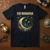 Black t-shirt with "Eid Mubarak" text and a golden crescent moon containing a mosque silhouette, surrounded by stars