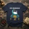 Eid Mubarak t-shirt with white text, crescent moon, mosque, and palm tree graphic in teal and gold