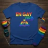 En Gay Ged text with rainbow colors and heart hands holding engagement ring graphic on blue t-shirt