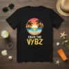 Black t-shirt with "Enjoy The Vybz" text and a tropical sunset beach graphic featuring palm trees and ocean waves