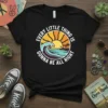 Black t-shirt with retro circular design featuring sunset, waves, palm trees, and text "EVERY LITTLE THING IS GONNA BE ALL