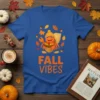 Blue t-shirt with orange text "FALL VIBES" and a cartoon hermit crab wearing a beanie surrounded by fall leaves and