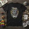 Black t-shirt with white and gold text "Family Requires Love Not DNA" in a circular puzzle design