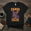 Fangs For The Coffee! text with a cute bat character holding a coffee cup on a black t-shirt