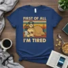 Sloth lying down with coffee and alarm clock, text "FIRST OF ALL I'M TIRED" on vintage background t-shirt
