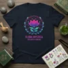 Flora Mystica Enchanted Gardens T-Shirt with a vibrant pink and purple lotus flower design inside a circular wreath