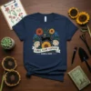 Navy t-shirt featuring a black cat surrounded by sunflowers, roses, and blue irises with "Floral Feline Fantastic Bloom & Grow"