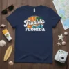 Navy blue t-shirt with retro "Florida FLORIDA" text, palm tree, sun rays, and ocean waves graphic