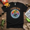 Black t-shirt featuring the "Florida Man" text above a cartoon alligator surfing a monster truck wheel in the ocean