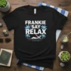 Black t-shirt with "Frankie Say Relax" text in white and blue palm trees, featuring a person relaxing by the water