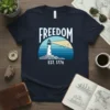 FREEDOM EST. 1776 text with a lighthouse graphic on a navy blue t-shirt, representing American independence
