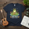 T-shirt design featuring a frog playing a banjo with "FROG ROCK SOUNDS OF THE SWAMP" text, surrounded by mushrooms and