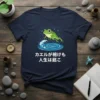 Japanese proverb "カエルが怖けも 人生は越こ" with a cute frog jumping in the rain and water ripples on a dark t-shirt