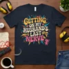 Graphic t-shirt with the quote "GETTING ON MY HUSBAND'S LAST NERVE" in retro fonts and colors, featuring a small devil