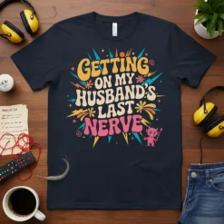 Graphic t-shirt with the quote "GETTING ON MY HUSBAND'S LAST NERVE" in retro fonts and colors, featuring a small devil