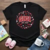Black t-shirt with "Gigi Est. 2026" text surrounded by a floral and heart wreath
