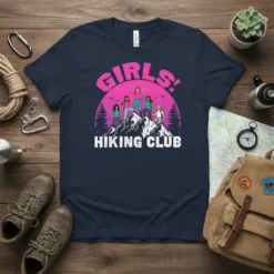 Girls Hiking Club t-shirt featuring five women celebrating on a mountain peak with pine trees and a sunset background