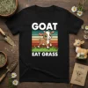 Black t-shirt with "GOAT EAT GRASS" text and a cartoon goat graphic, set against a retro striped background