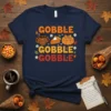 Gobble Gobble Gobble text with a cute turkey, slice of pie, and pumpkin graphic on a navy t-shirt for Thanksgiving