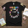 Black t-shirt with colorful "God Says I Am" text and a circular design of affirmations including Love, Strong, Empowered, Chosen