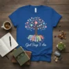 Blue t-shirt with "God Says I Am" text, a tree with colorful flowers, and roots labeled with affirmations like Forgiven