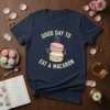 Good Day To Eat A Macaron text with stacked pink, white, and yellow macarons graphic on a navy t-shirt