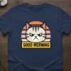 Grumpy cat face with "GOOD MORNING" text on a navy blue t-shirt, retro sunset background