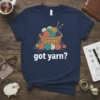Got Yarn? text with a basket of colorful yarn balls and knitting needles graphic on a navy t-shirt