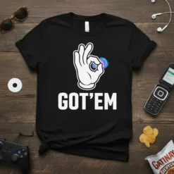 Black t-shirt with white "GOT'EM" text and a white hand making an OK sign with a colorful object in the