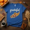 Blue t-shirt with the word "grateful" in cursive and a cornucopia overflowing with colorful autumn fruits and vegetables