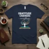 Gratitude Changes Everything quote with a tree growing from an open book, birds flying out, on a navy t-shirt