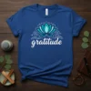 Blue t-shirt with the word "gratitude" in white script and a teal lotus flower graphic above