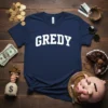 Navy blue t-shirt with "GREDY" in bold white collegiate font, surrounded by props symbolizing wealth like gold coins and money