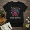 Black t-shirt featuring the text "GROWING LOVE WITHIN" above a colorful anatomical heart with roses and vines