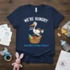 Pregnancy announcement t-shirt with text "WE'RE HUNGRY Guess Who's Coming to Dinner?" and a stork carrying a basket of food