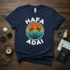 Navy blue t-shirt with "Hafa Adai" text and a colorful sunset graphic with palm trees, representing Guam souvenir