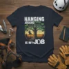 T-shirt with white text "HANGING AROUND IS MY JOB" and a graphic of a person on a swing under a