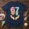 Navy t-shirt with the number 67 depicted as ice cream cones and donuts, held by hands, with sprinkles falling
