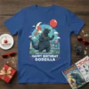 Happy Birthday Godzilla T-Shirt featuring a cartoon Godzilla holding a balloon and wearing a party hat, with a city skyline