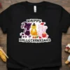 Happy Hallothanksmas text with three cartoon cats dressed for Halloween, Thanksgiving, and Christmas on a black t-shirt