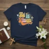 Retro style "He is Risen" text with a dove and cross graphic on a navy t-shirt