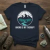 Hiking Is My Therapy quote on a navy t-shirt with a circular mountain and forest graphic