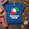 Holiday Crew text with three stacked elf hats in red, white, and green on a blue t-shirt