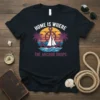 Nautical t-shirt with "Home Is Where The Anchor Drops" quote, featuring a sailboat, anchor, and palm trees at sunset