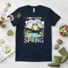 Hop Into Spring t-shirt design featuring a cute frog on lily pads with colorful text and floral accents