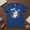 A blue t-shirt with the text "HUH?" and a cartoon cat in an astronaut suit floating in space
