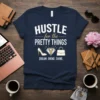 Navy t-shirt with "Hustle for the Pretty Things Dream Grind Shine" text and graphics of a high heel, diamond, and
