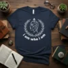 Navy blue t-shirt with white text "i am who i am" inside a laurel wreath surrounding a profile of a