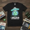 T-shirt with "I BELIEVE UFO ALIENS SPACE" text and cartoon aliens emerging from a UFO